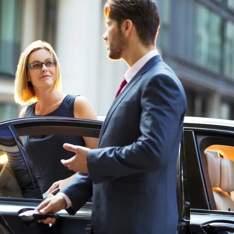 Homme en costume ouvrant la porte d'une voiture pour une femme.